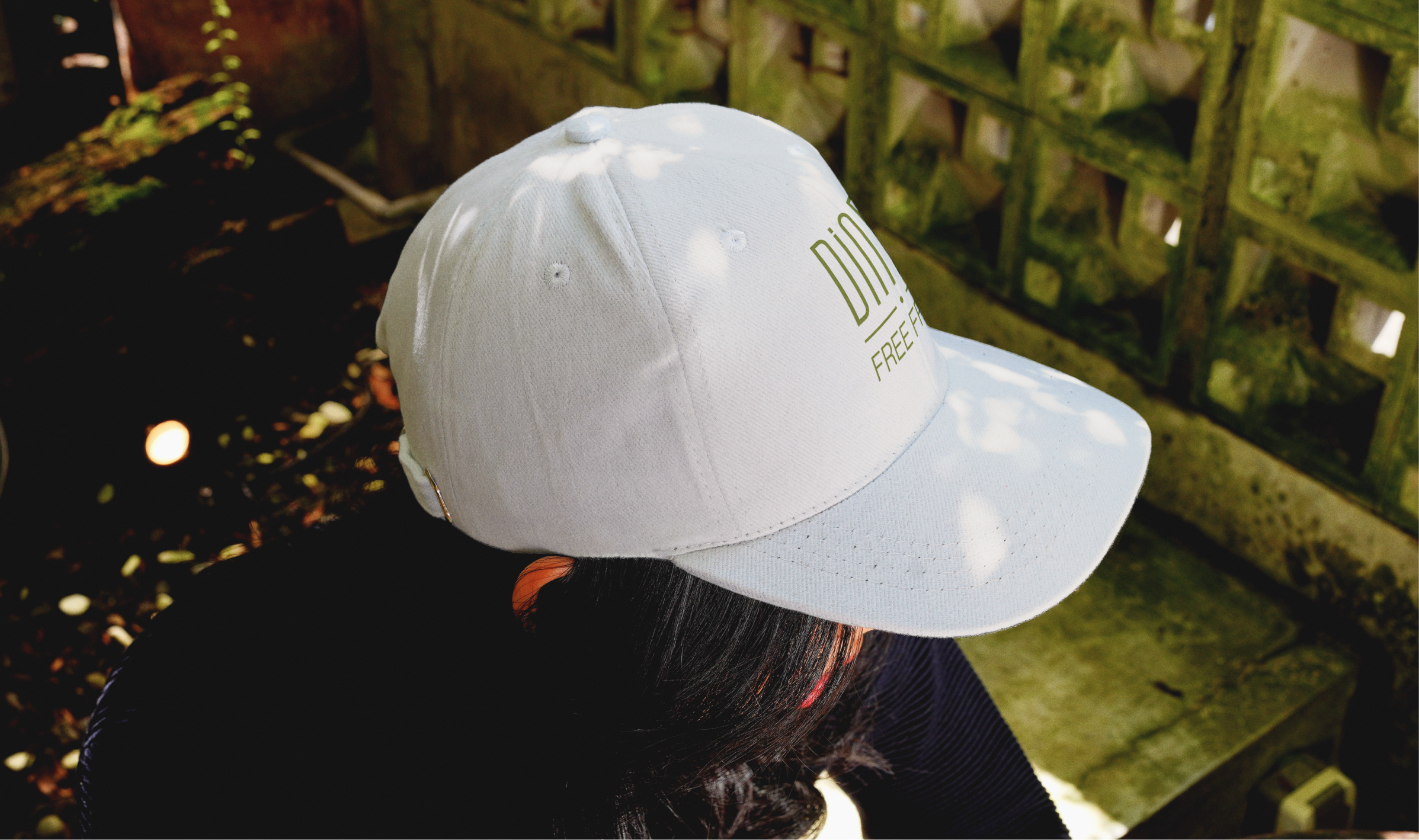 Close-up of a person wearing a white cap embroidered with the Diner Free From logo, outdoors