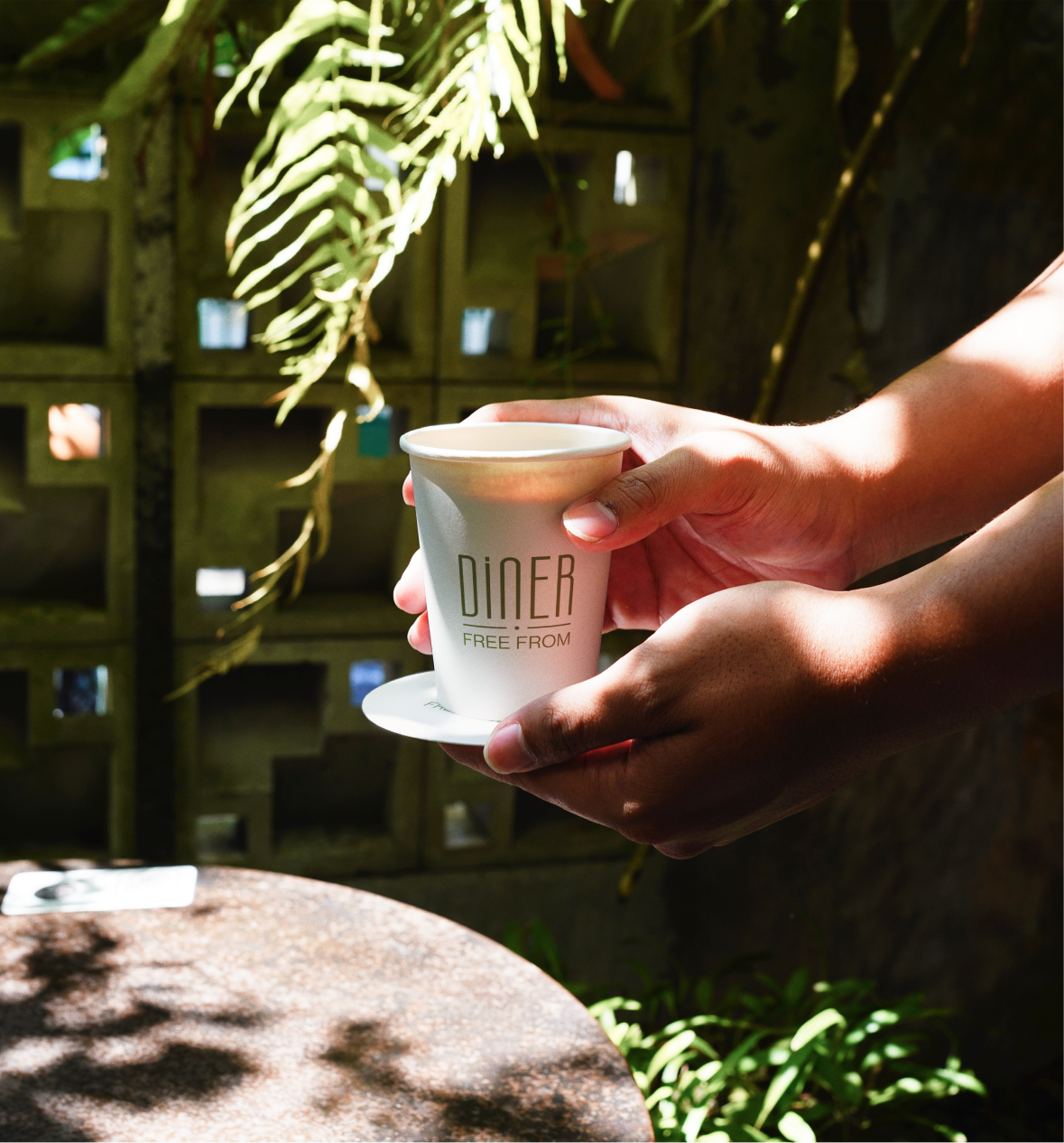 Hands passing a Diner Free From branded coffee cup outdoors