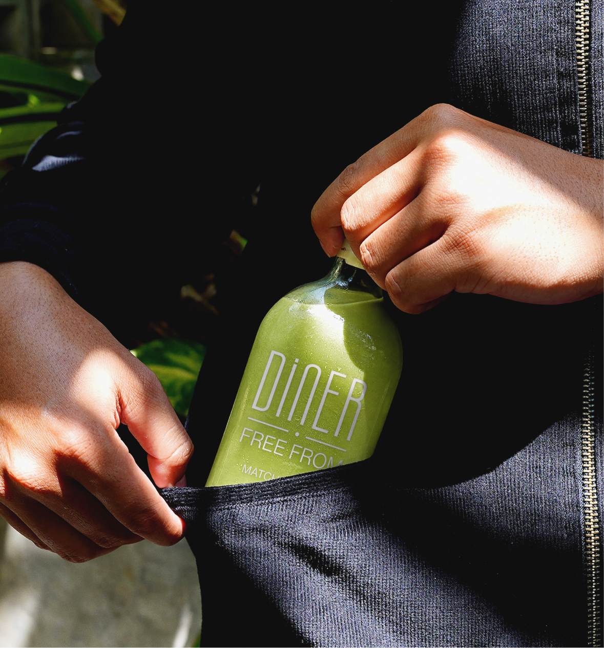 Close-up of hands pulling a Diner Free From branded matcha drink from a jacket pocket