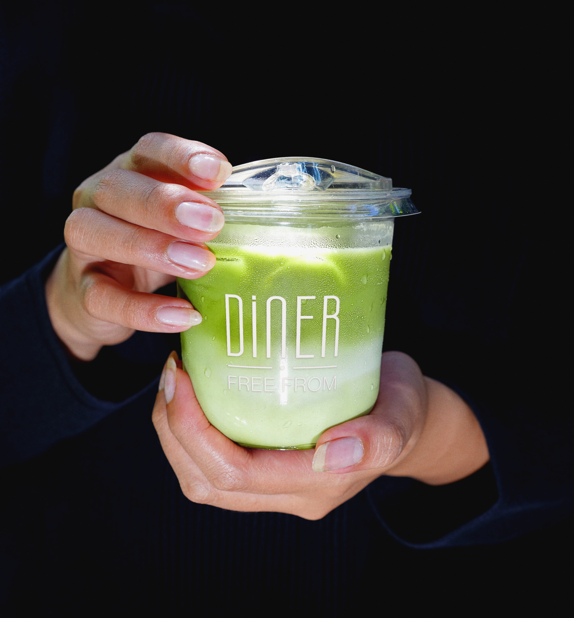 Close-up of hands holding an iced matcha drink in a Diner Free From branded cup
