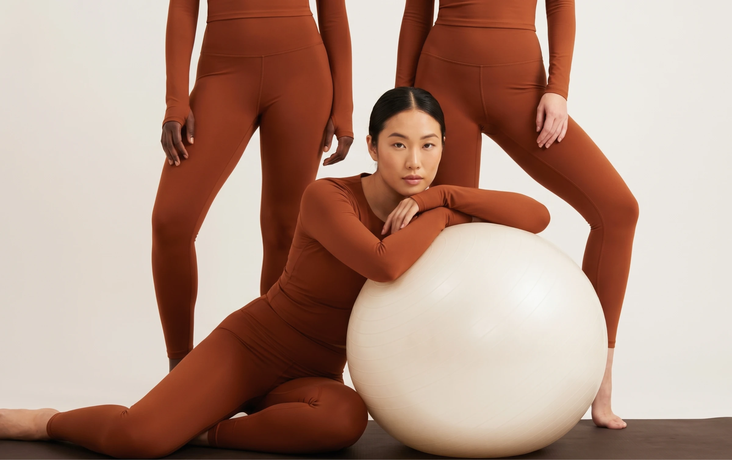 HOH 1 Three models in matching terracotta activewear, one leaning on a large exercise ball