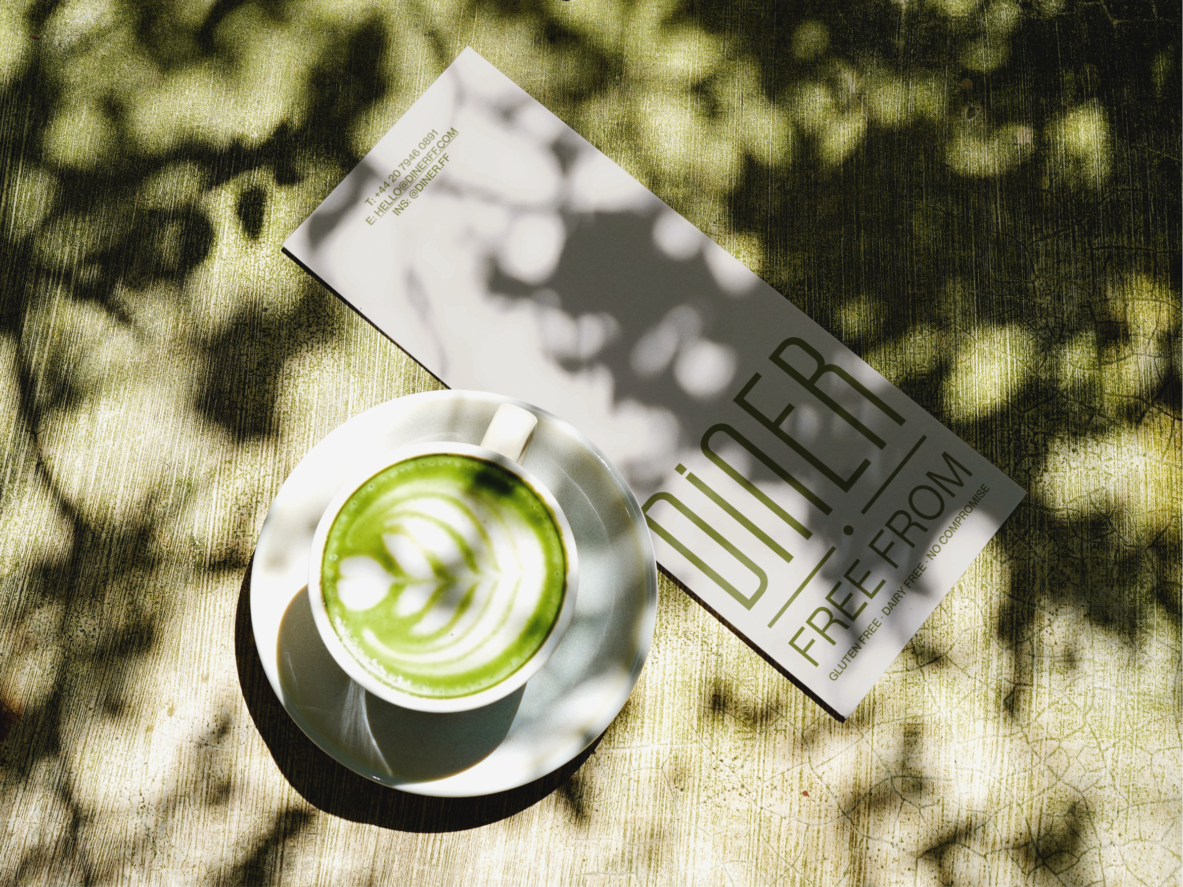 Overhead shot of a matcha latte and a Diner Free From branded menu leaflet on a sunlit table (this file is currently used twice on the page, worth checking if that's intentional)