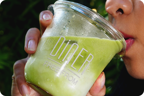 Close-up of a woman drinking a green smoothie from a Diner Free From branded jar (next project link)