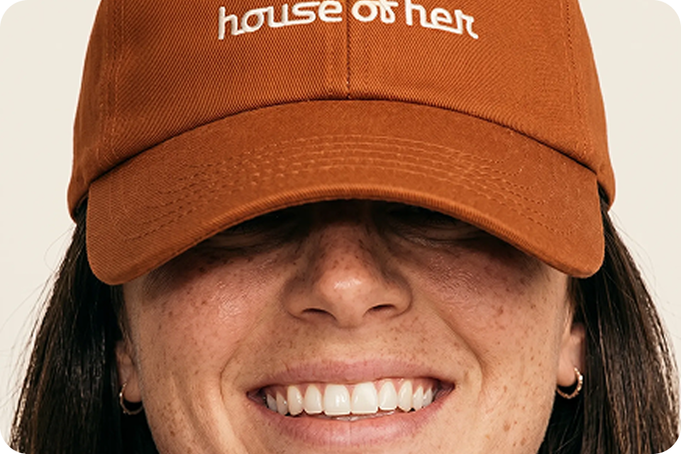Close-up of a smiling woman wearing a House of Her branded cap (next project link)