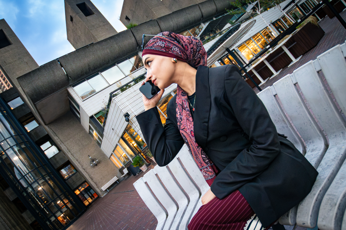 Close-up profile of a woman holding a phone to her ear, Barbican terrace behind her