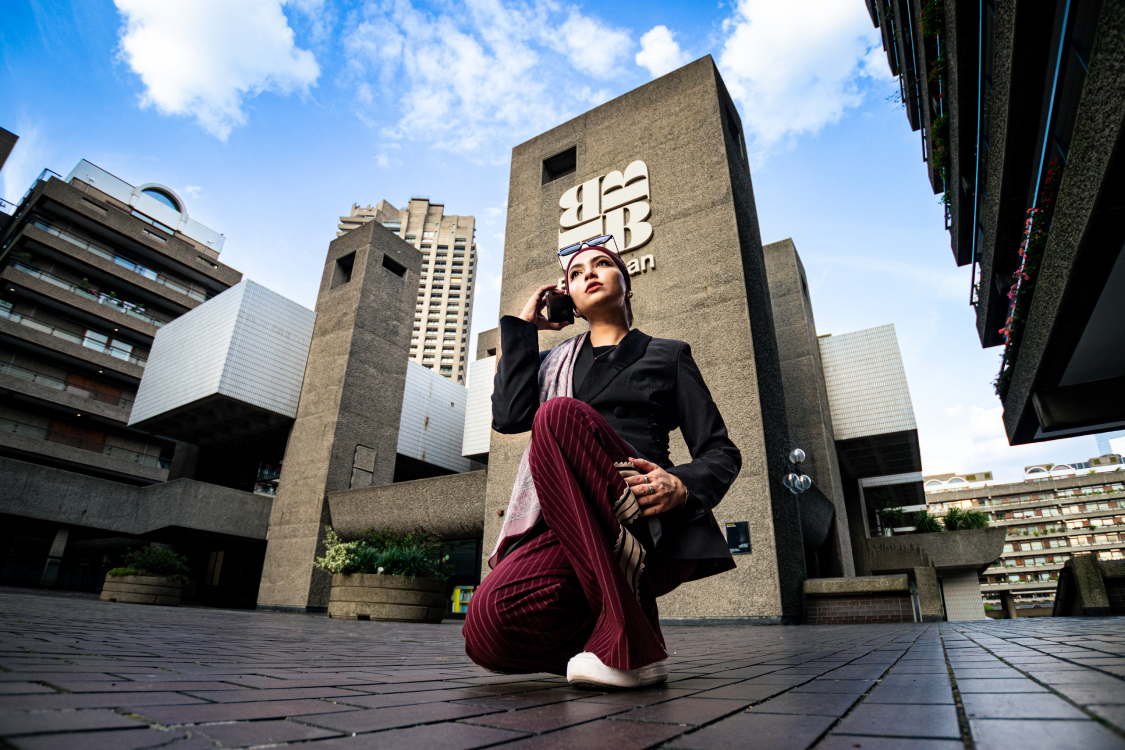 Over-the-shoulder shot of a woman photographing the Barbican Centre on her phone